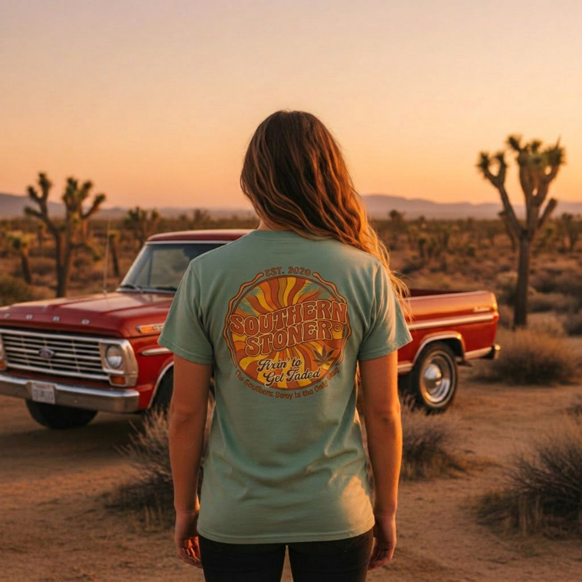 Woman wearing sage Fixin’ to Get Faded Retro Sun Tee beside a red pickup at sunset, back view
